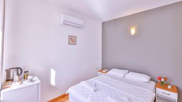 Habitación de hotel con cama, mesita de noche y un pequeño escritorio con tetera, taza de café y tarro.
