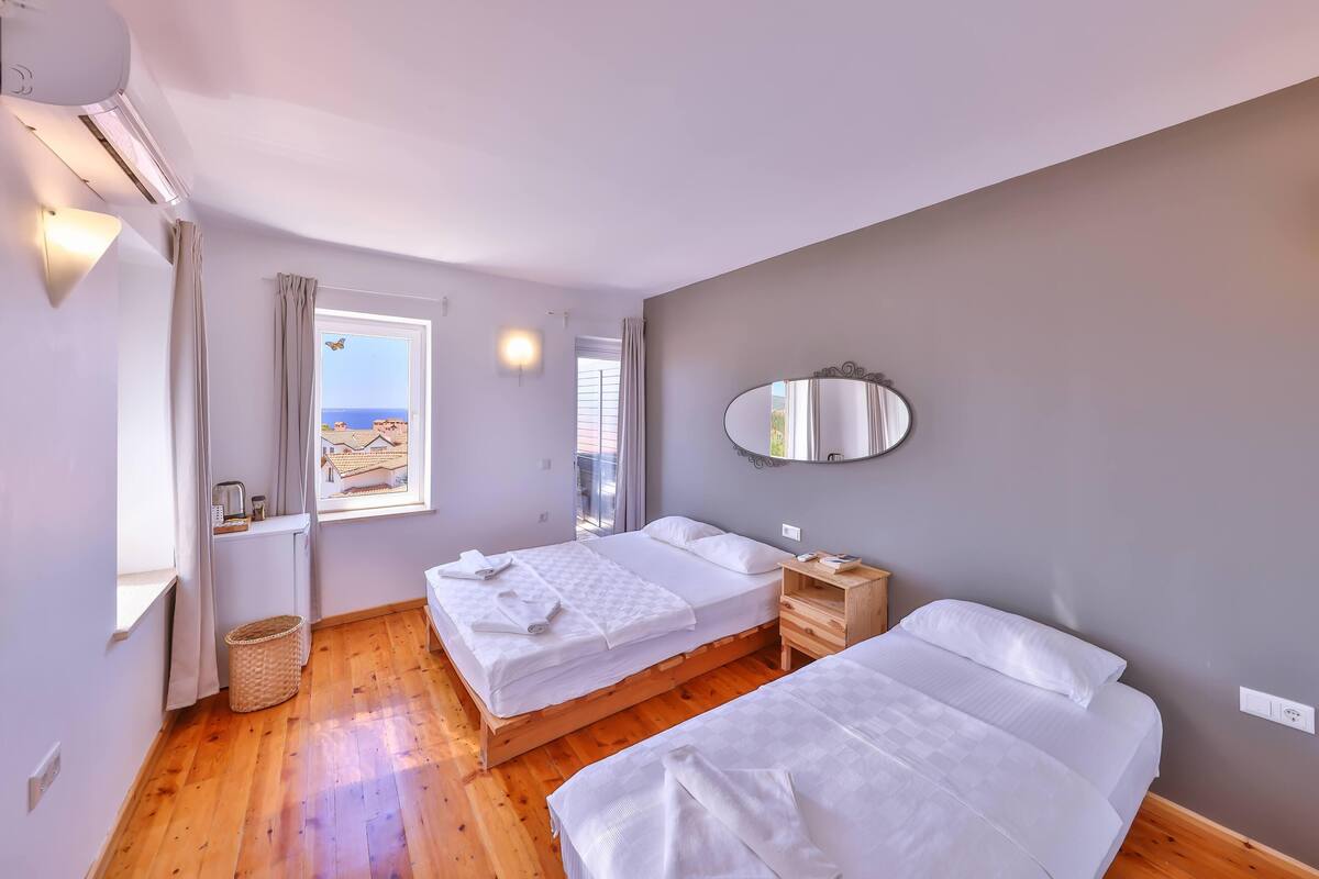 A bedroom with two beds, a window with curtains, a mirror, a bedside table, and a ceiling fan.