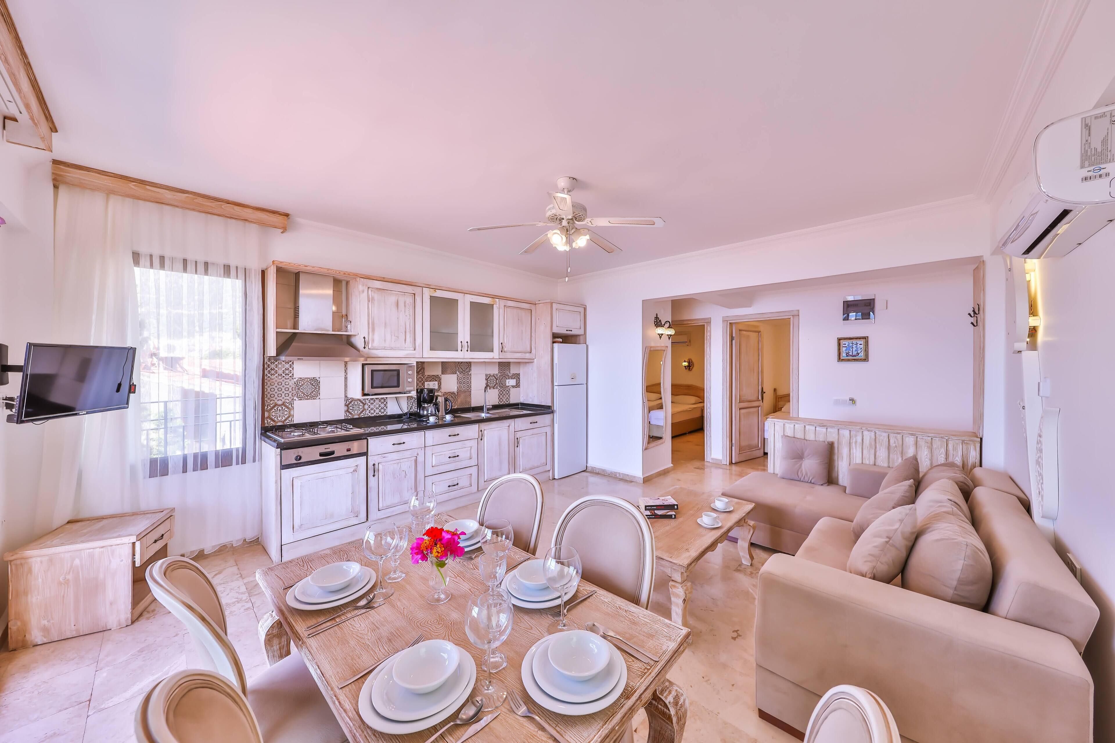 Una cocina moderna con armarios blancos, una mesa de comedor con platos y vasos, y un sofá beige en la sala de estar.
