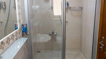 Un baño con ducha envuelta en vidrio, un lavabo y un espejo.