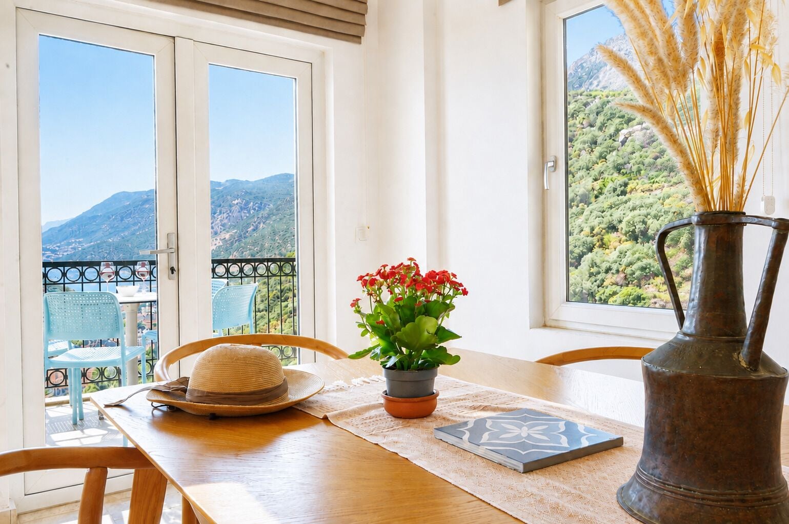 Un balcón con una mesa, sillas, una planta en maceta, un jarrón y vistas de un paisaje montañoso.