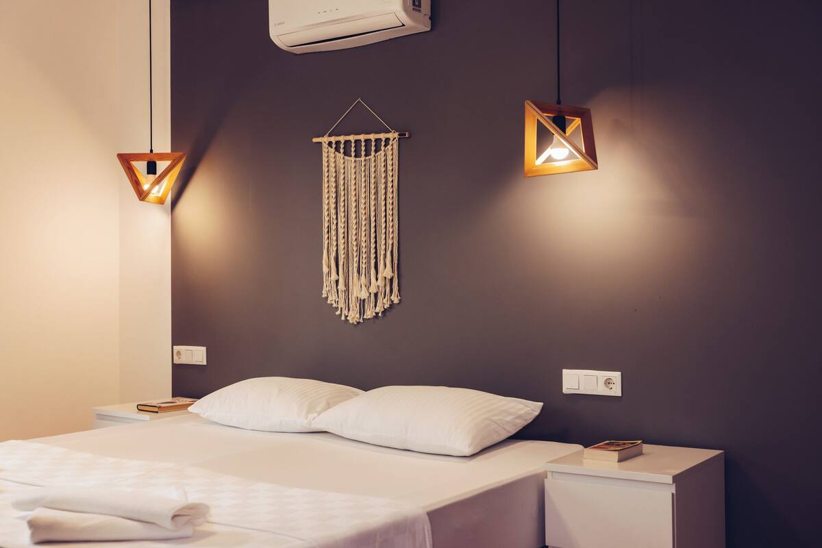 A modern bedroom with a bed, bedside tables, a wall-mounted air conditioner, and two pendant lights.
