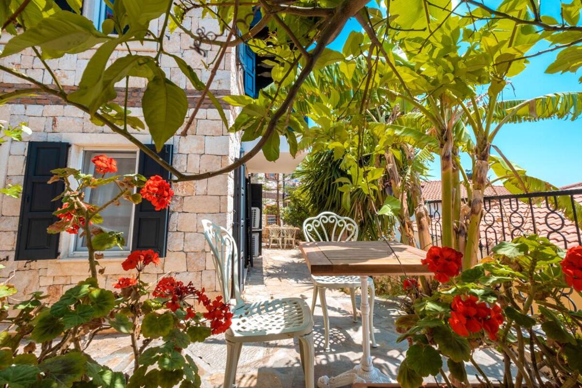 A patio with a table and chairs, surrounded by red flowers and greenery.