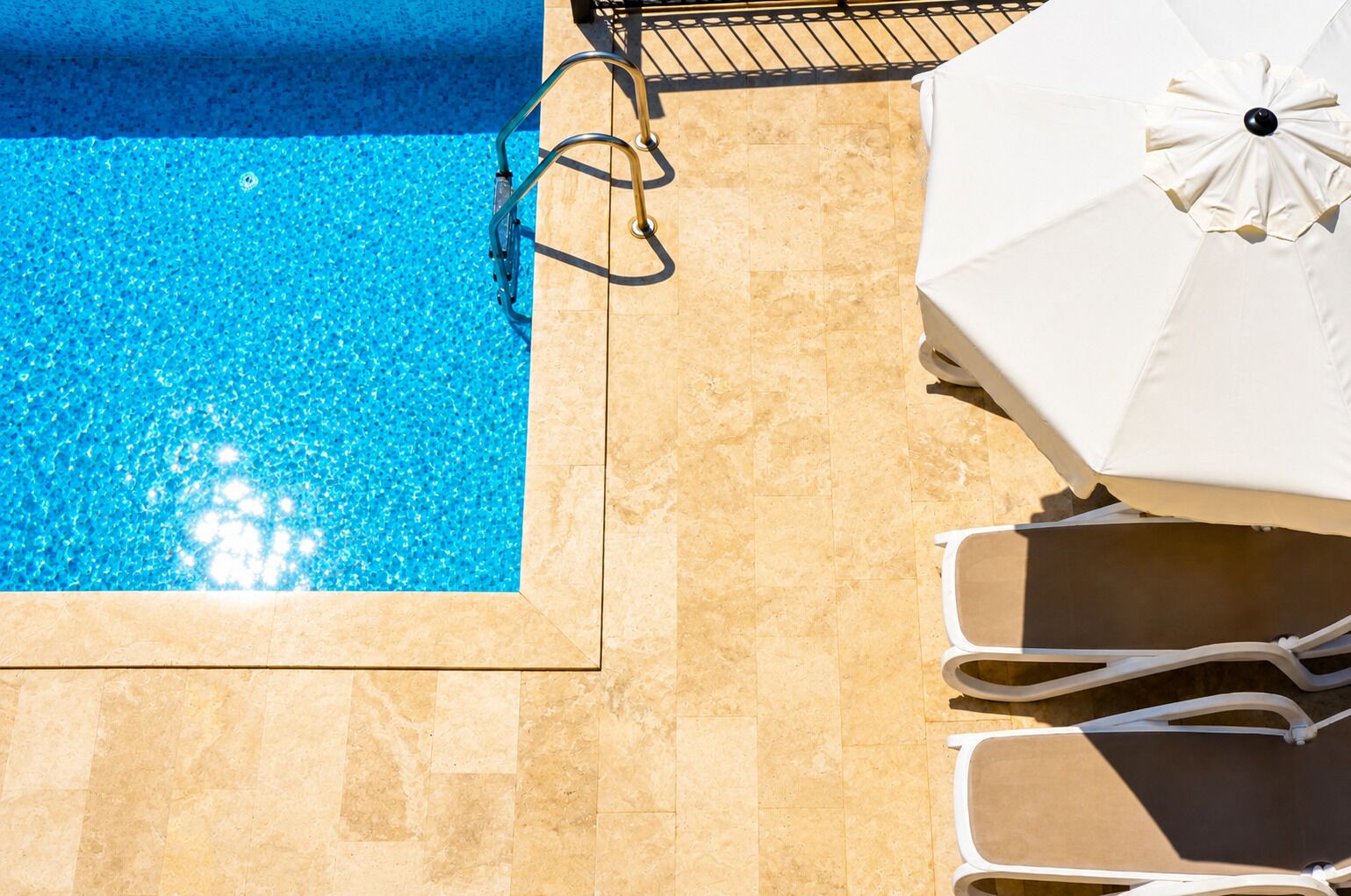 A swimming pool with a tiled edge, a metal pool ladder, and a white umbrella.