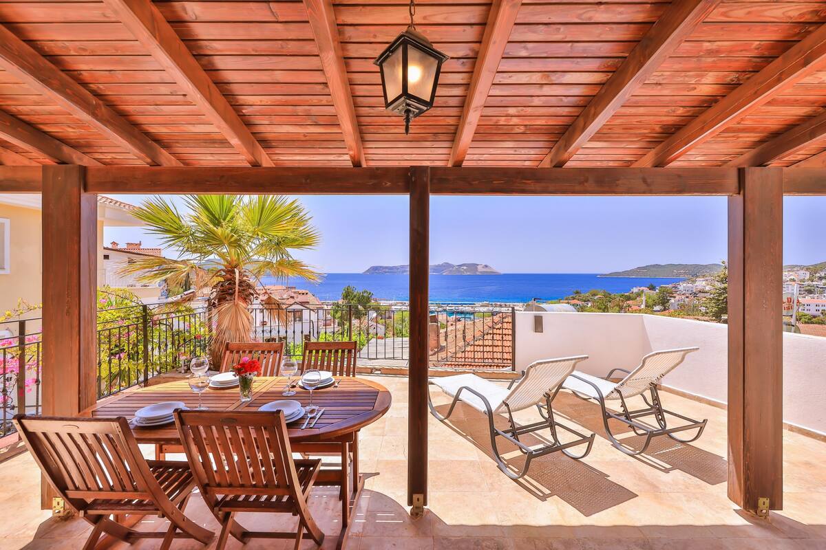 A wooden pergola with a table and chairs, overlooking a coastal view.