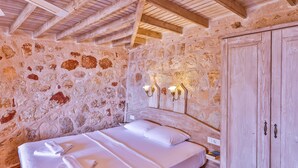 A bedroom with a stone wall, wooden beams, a bed with white linens, and a wooden wardrobe. - Hotel Luna Kas (Kas)