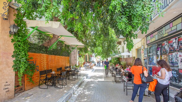 An outdoor café with tables and chairs, a brick wall, and greenery. - Raise Rooms in Center of Athens (Athens)