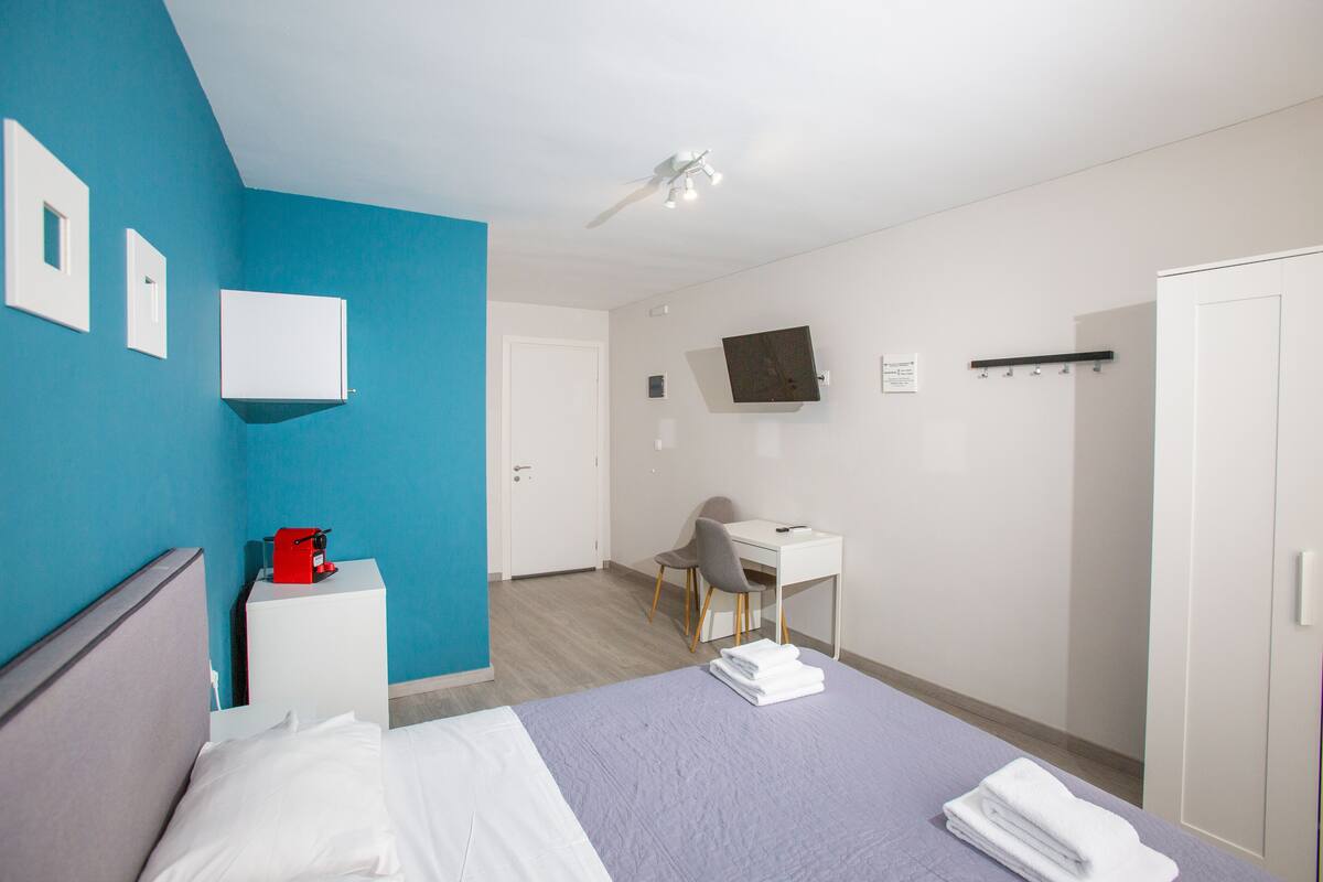 A hotel room with a bed, a desk, a chair, a TV, and a wardrobe.