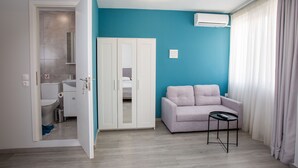 A modern room with a teal accent wall, a white wardrobe, a grey sofa, and a small table. - Raise Rooms in Center of Athens (Athens)