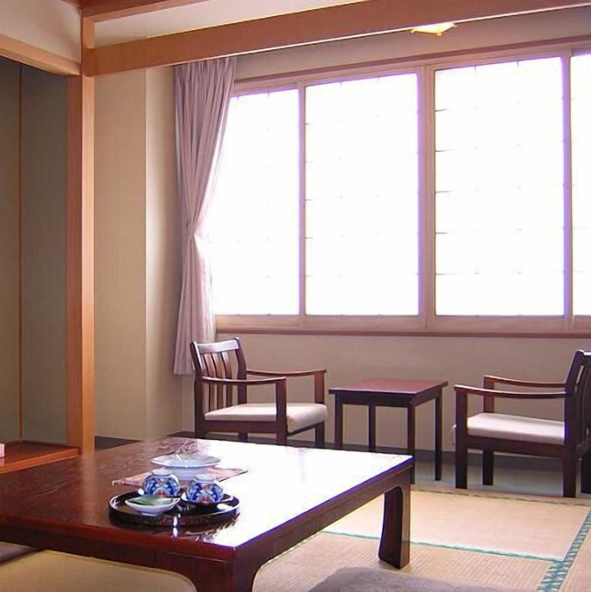 Una habitación con una mesa de madera, dos sillas, una mesita y una ventana con cortinas.