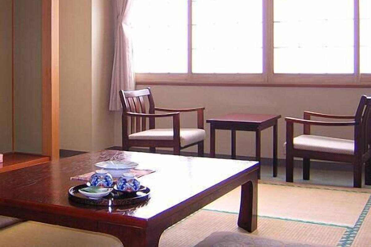 A room with a wooden table, two chairs, a small table, and a window with curtains.