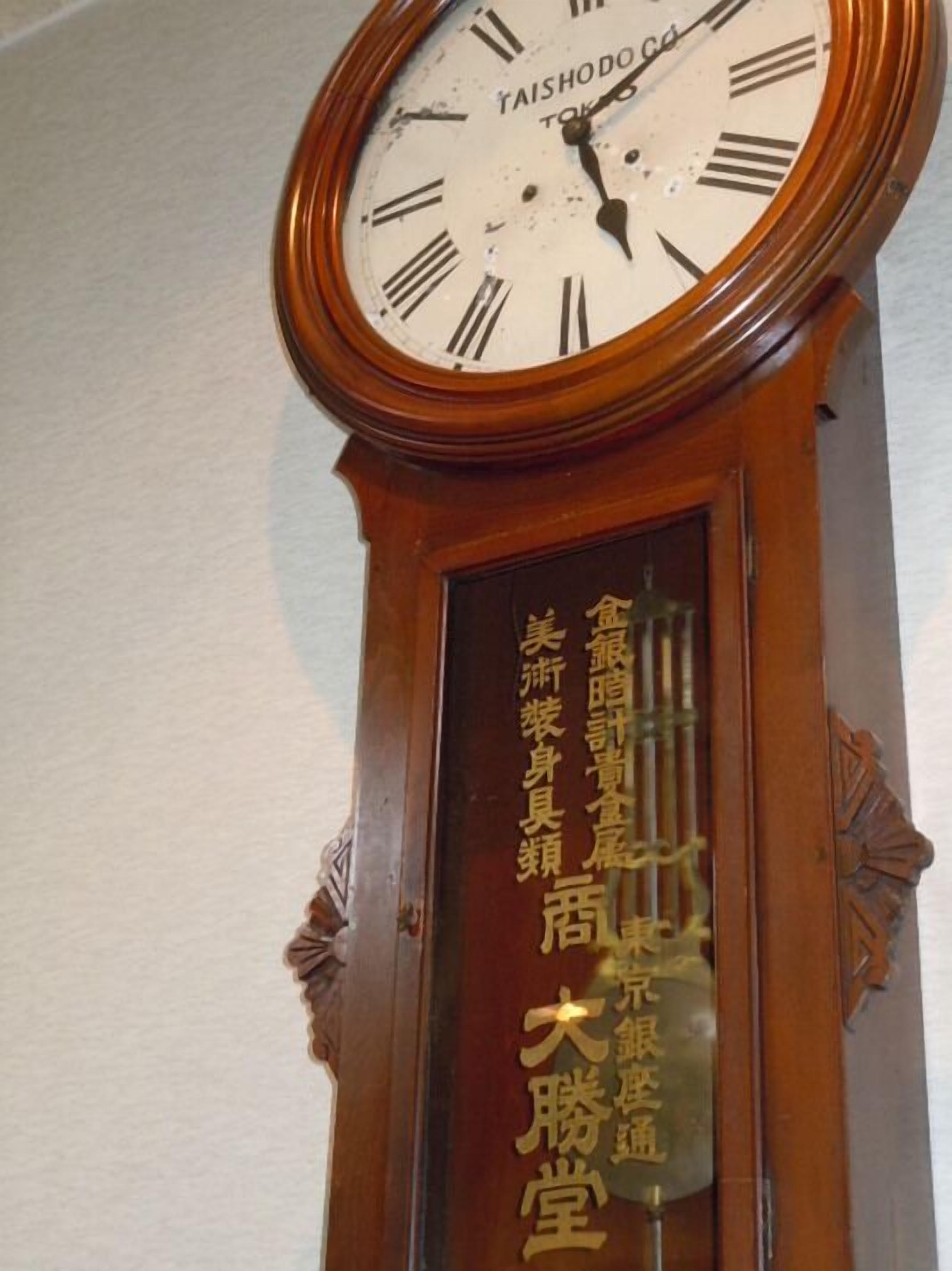 A wall-mounted clock with Roman numerals and a wooden frame.
