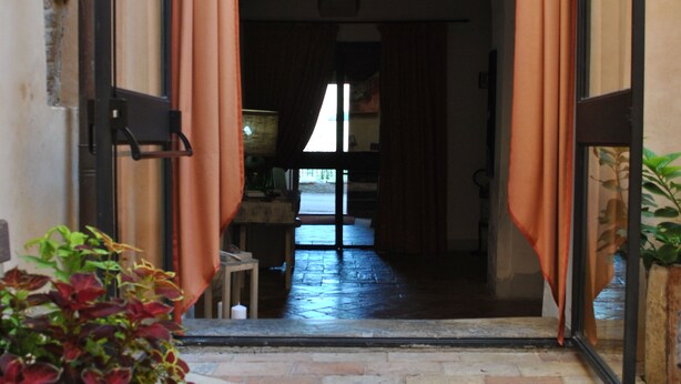 A corridor with a brick floor, an archway with draped fabric, and a potted plant. - Palazzo Bonfranceschi (Belforte del Chienti)
