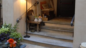 A stone archway leading to a staircase with a lamp and wicker furniture. - Palazzo Bonfranceschi (Belforte del Chienti)