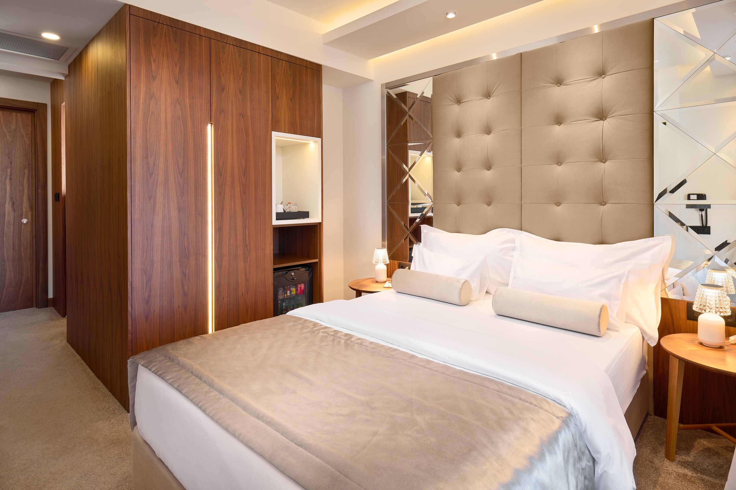 A hotel room with a large bed, a wardrobe, a mirror, and a bedside table with a lamp.