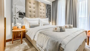 Ein modernes Hotelzimmer mit einem großen Bett, einem Nachttisch aus Holz und einem Spiegel mit geometrischen Mustern.