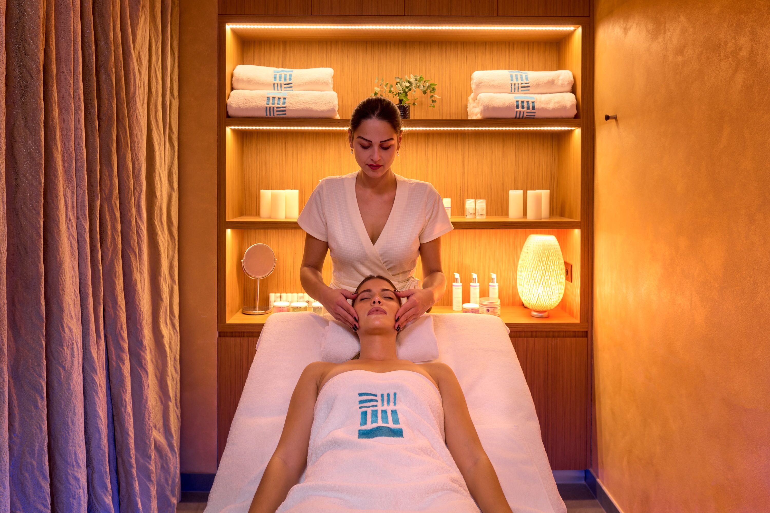 A massage therapy room with a wooden shelf containing towels and toiletries.