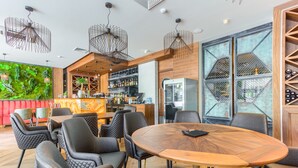 Ein modernes Restaurant mit Barbereich, Sitzgelegenheiten mit gepolsterten Stühlen und einem großen Holztisch.