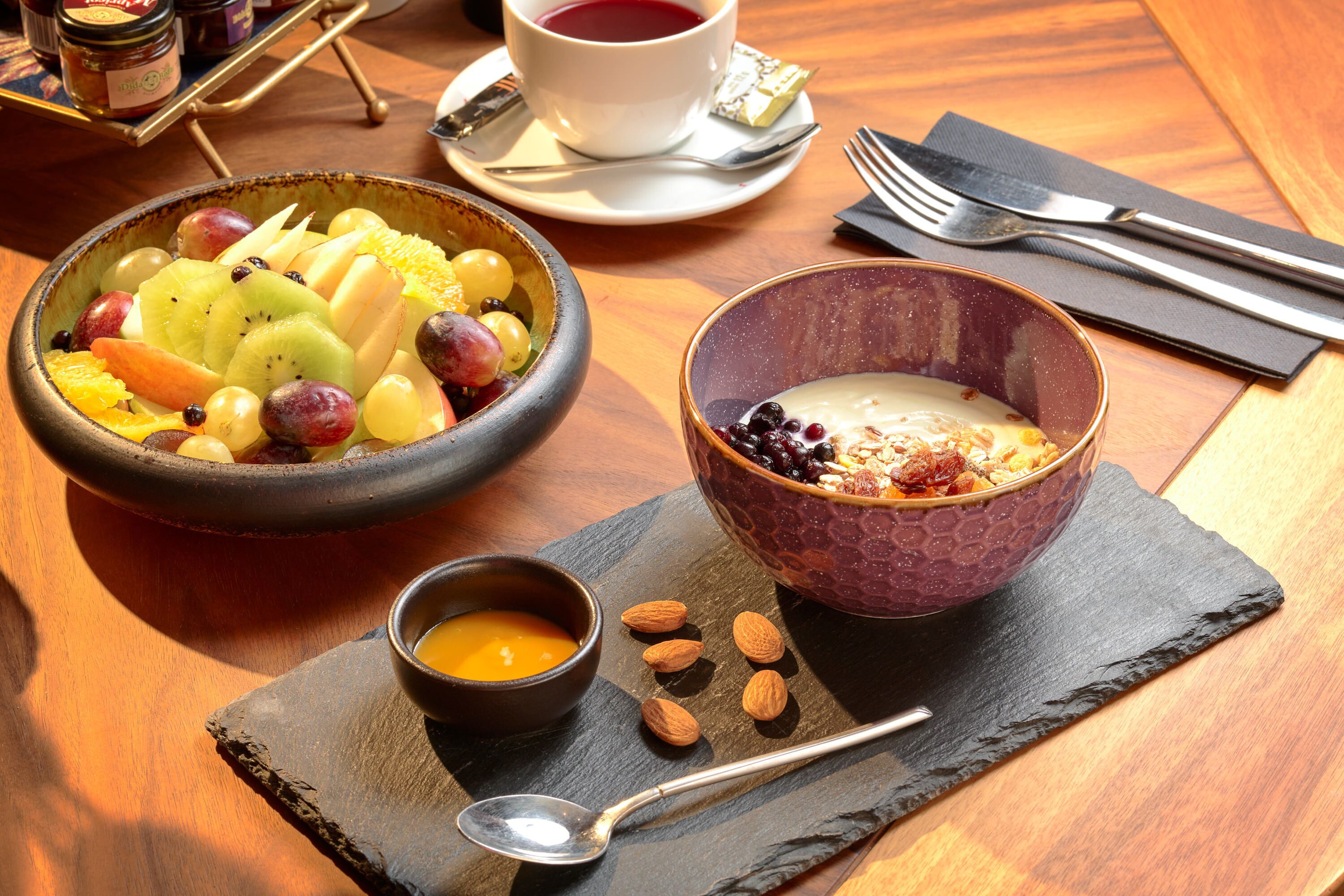 Ein Frühstückstisch mit Obstschale, Joghurt mit Beeren und einer kleinen Teetasse sowie einem Honigschälchen.