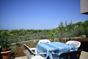A patio with a table covered in a blue tablecloth, white chairs, and a potted plant. - Apartment Lucy (Krk)