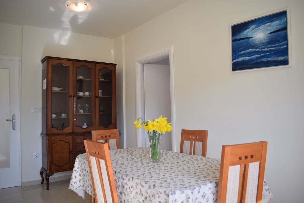 A dining area with a table set for two, a wooden cabinet, and a painting on the wall.