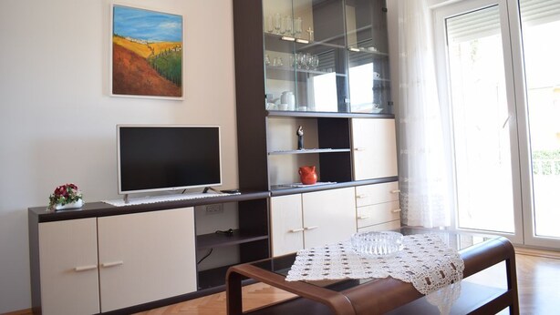 Una sala de estar moderna con un televisor de pantalla plana, un aparador de vidrio con vajilla y un cuadro en la pared.