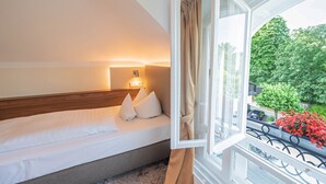 A hotel room with a bed, a nightstand, a window with curtains, and a view of greenery outside. - Hotel Villa am Kurpark (Bad Homburg v.d. Hoehe)