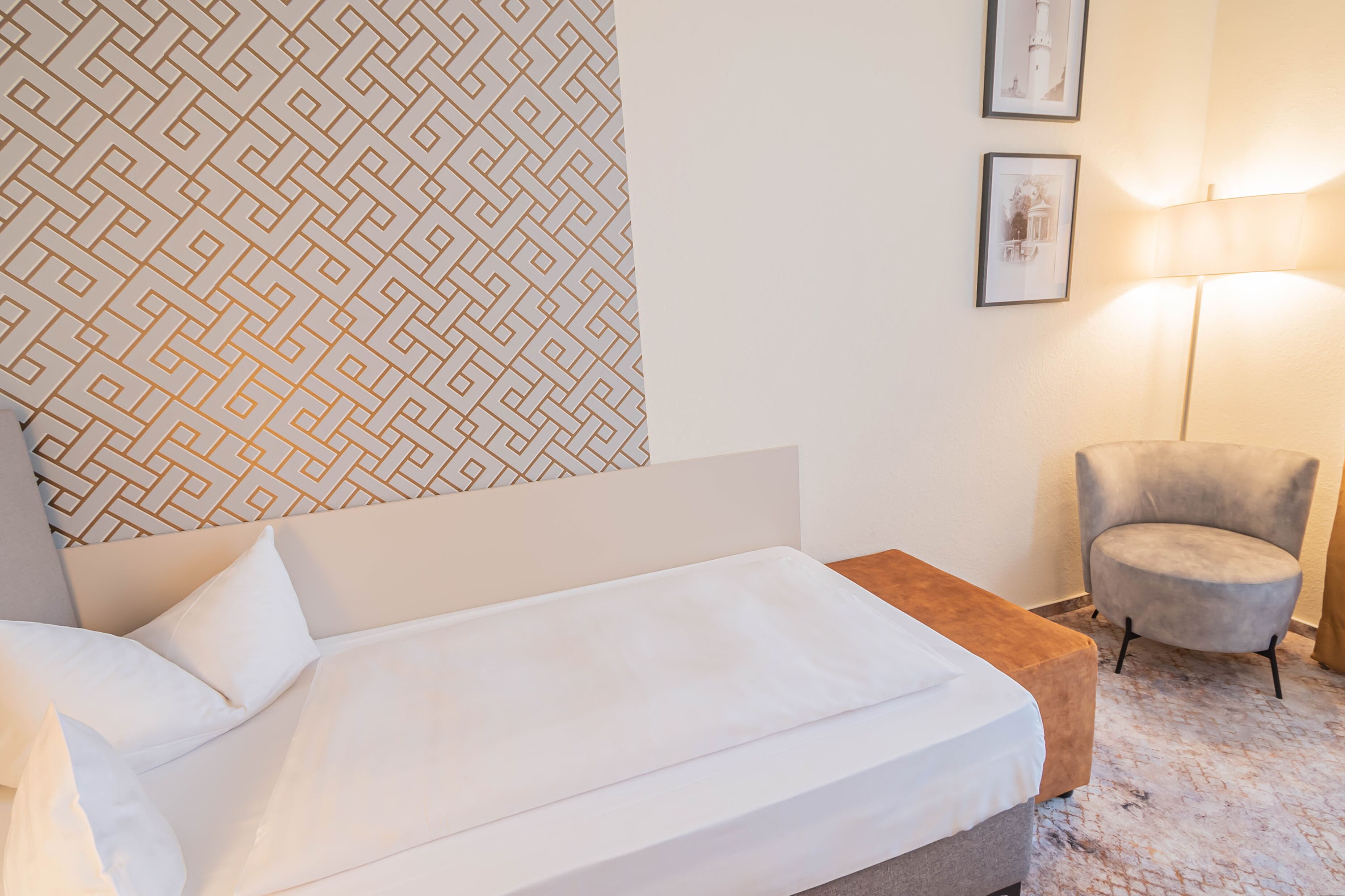 Ein Hotelzimmer mit einem Bett, einem Nachttisch, einem Sessel und einer Wand mit Muster.