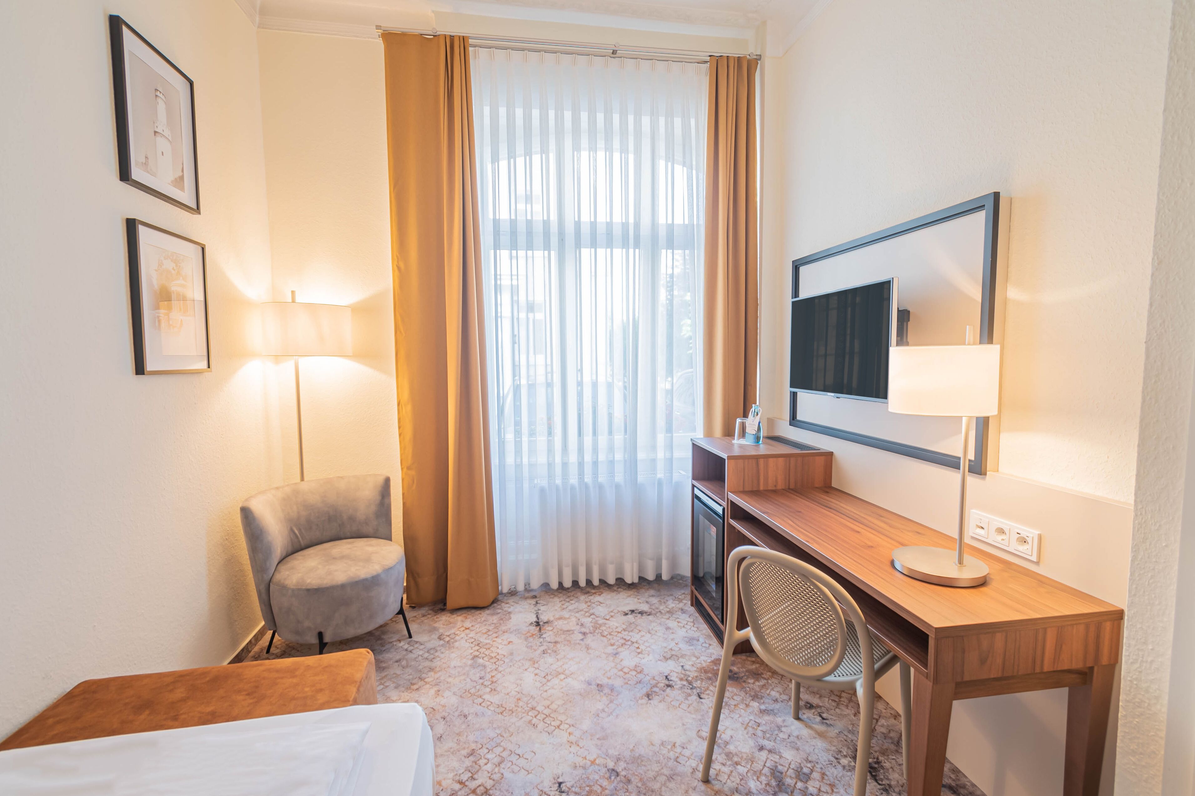 Ein Hotelzimmer mit Bett, Schreibtisch, Stuhl, Fernseher, Lampe und einem Fenster mit Vorhängen.