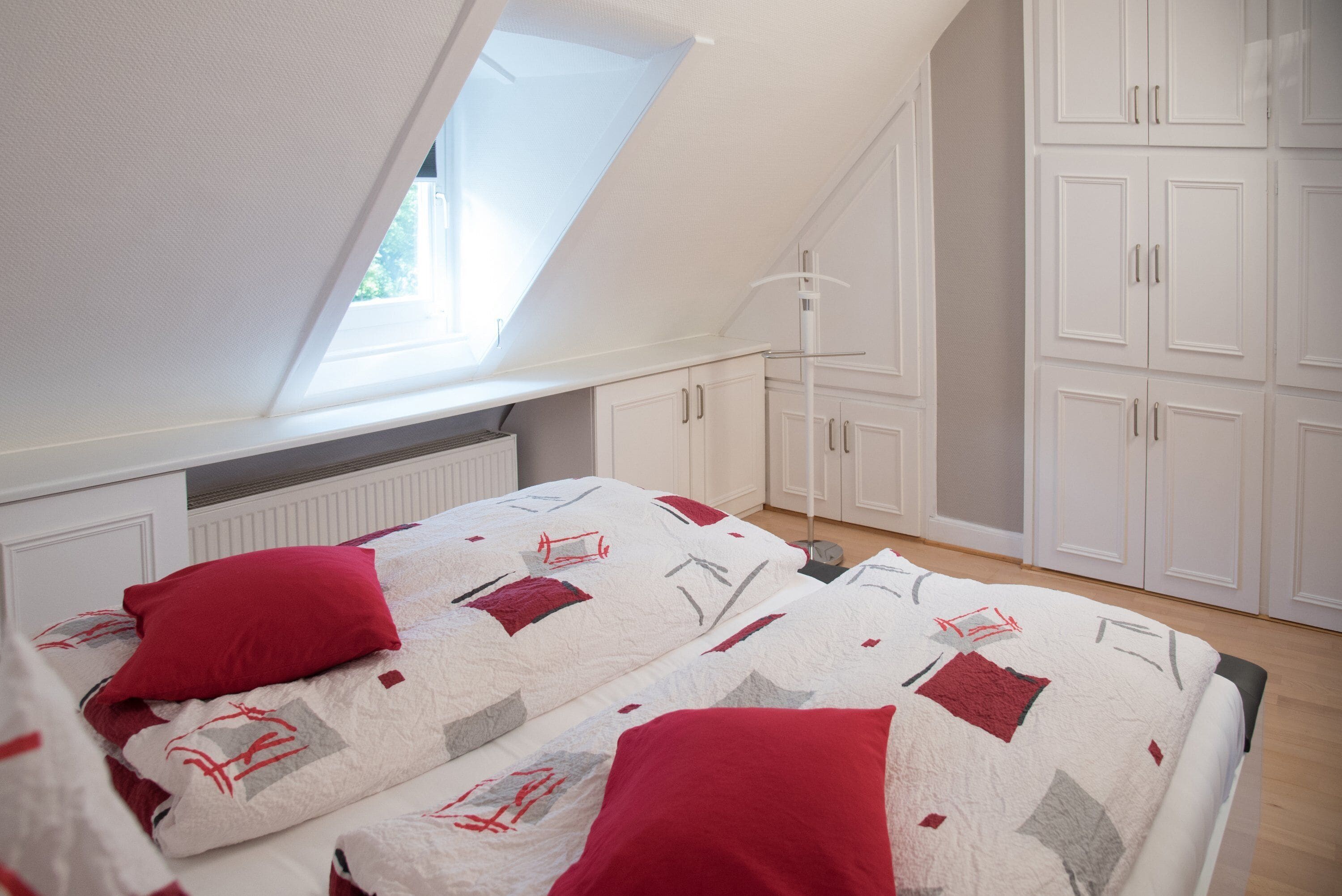 A bedroom with a sloped ceiling, a bed with a patterned duvet, and white cabinets.