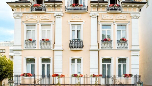 A large, elegant building with multiple balconies, a central staircase, and a well-maintained garden with a fountain. - Hotel Villa am Kurpark (Bad Homburg v.d. Hoehe)