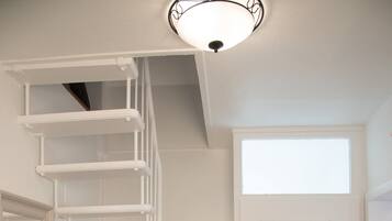 Un escalier menant à un deuxième étage, une porte blanche et un coussin rouge posé sur un meuble blanc.