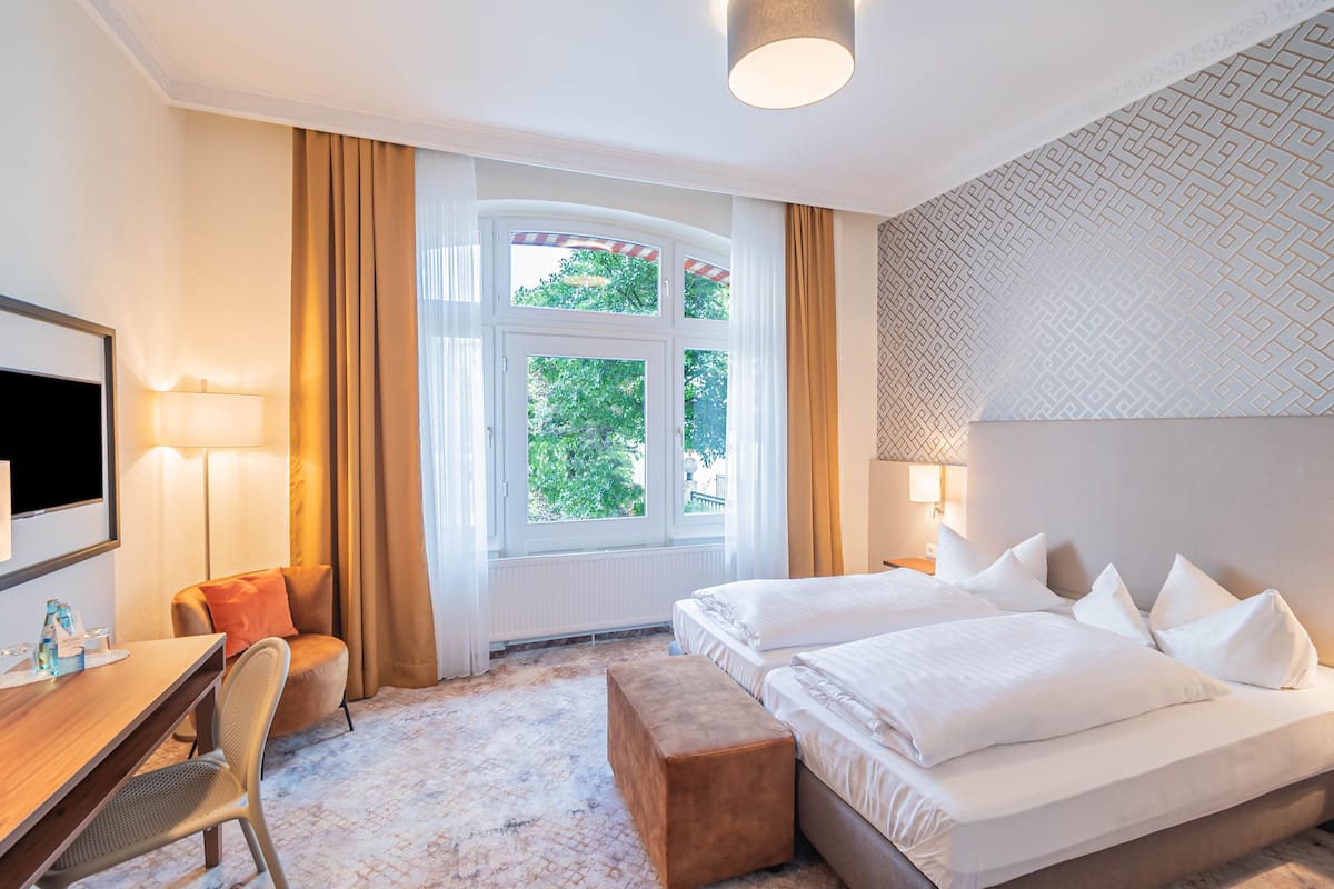 A hotel room with a large bed, a desk with a chair, a TV, and a window with curtains.