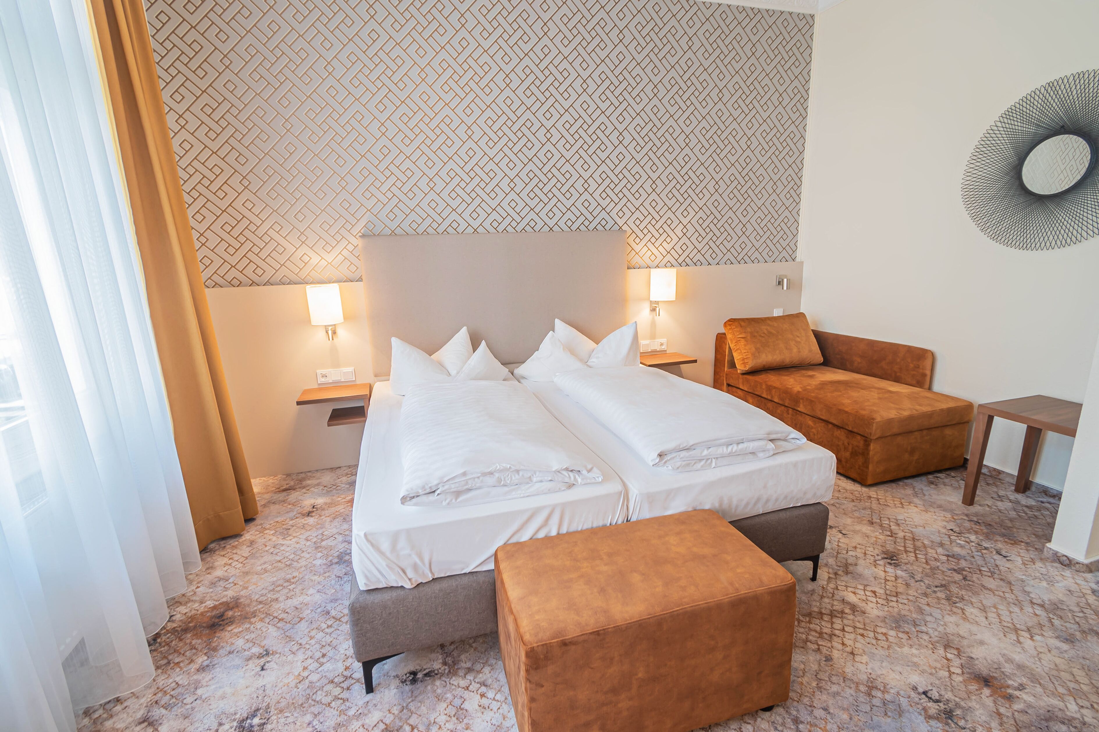 A hotel room with two beds, a sofa, a small table, and a patterned wall.