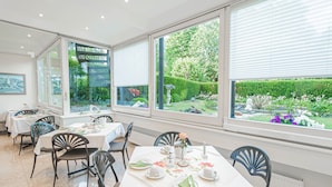 A dining area with tables set for a meal, large windows offering a view of a garden, and a modern interior design. - Hotel Villa am Kurpark (Bad Homburg v.d. Hoehe)