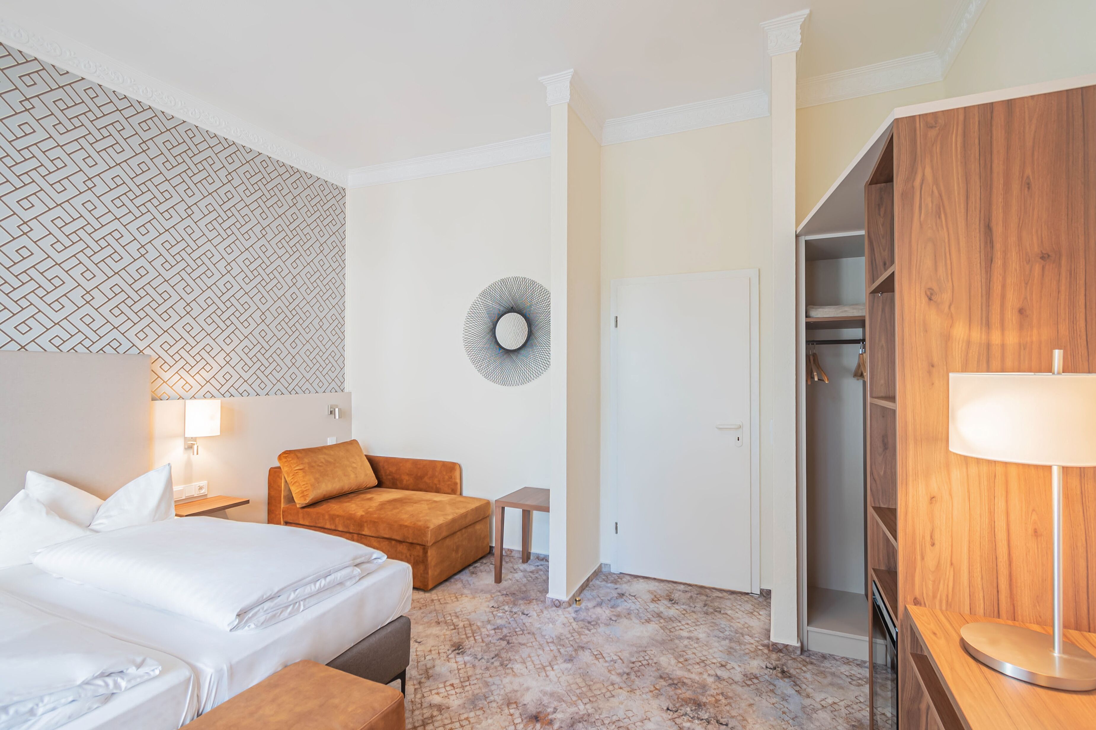 A hotel room with a bed, a sofa, a small table, a lamp, and a wardrobe.