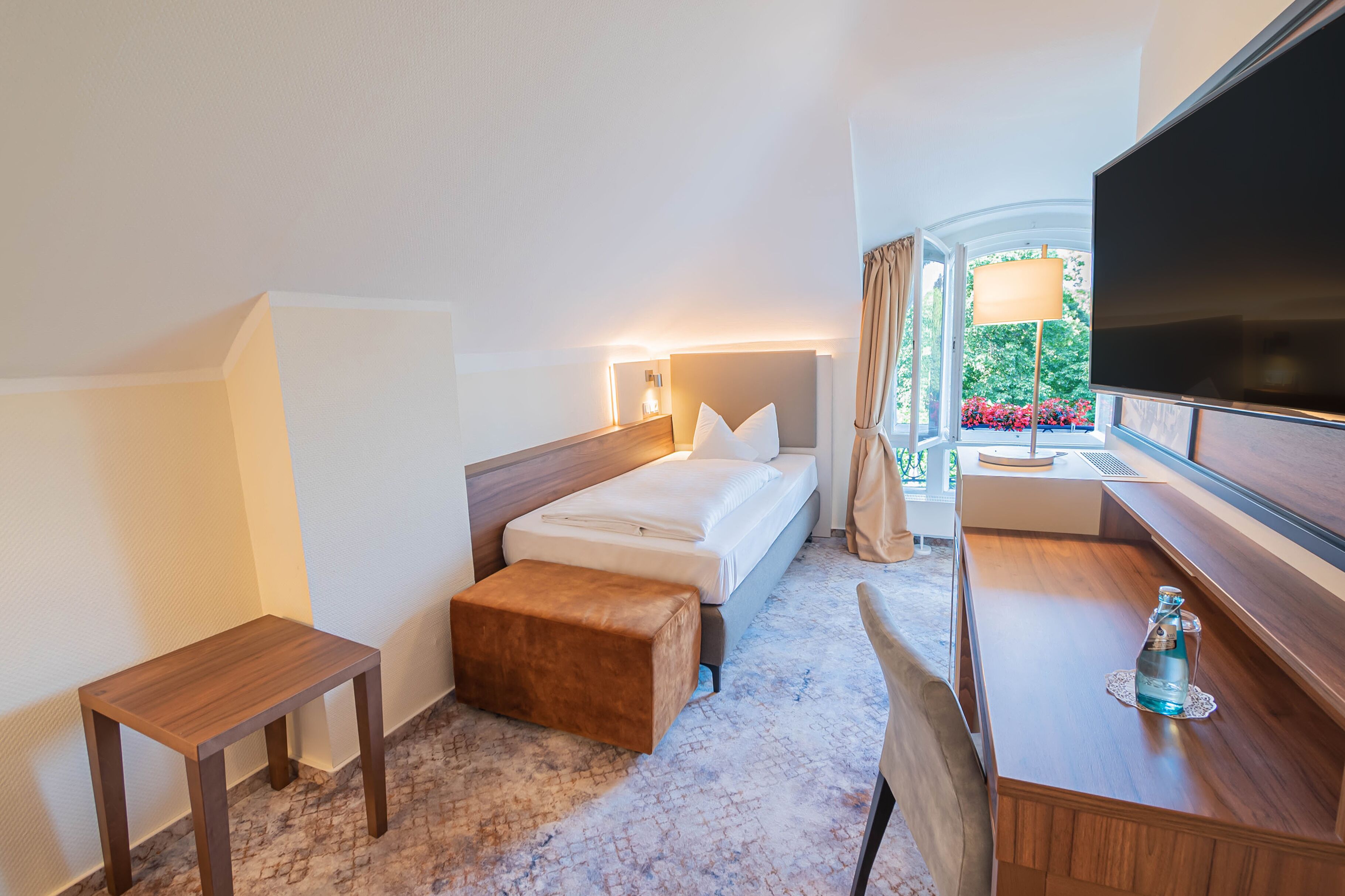 A hotel room with a bed, a desk, a TV, and a window with curtains.