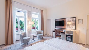 A hotel room with a bed, two armchairs, a desk with a television, and a refrigerator. - Hotel Villa am Kurpark (Bad Homburg v.d. Hoehe)