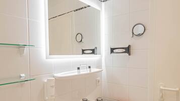 Un baño moderno con lavamanos blanco, espejo y estantes de vidrio.