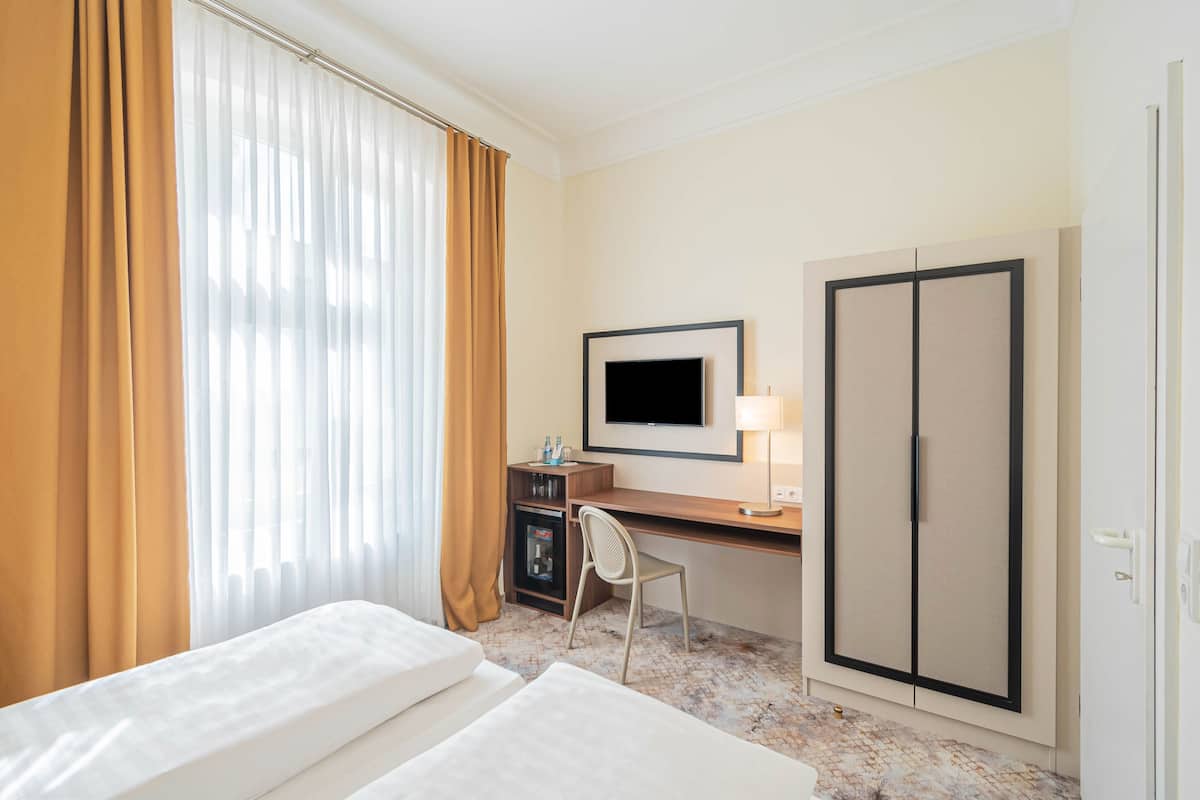 A hotel room with a bed, desk, chair, TV, wardrobe, and a minibar.