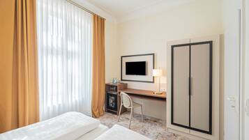 Ein Hotelzimmer mit Bett, Schreibtisch, Stuhl, Fernseher, Kleiderschrank und einer Minibar.