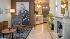 A hotel lobby with a reception desk, a large framed portrait, a fireplace, and two small tables with vases. - Hotel Villa am Kurpark (Bad Homburg v.d. Hoehe)