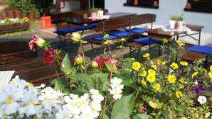 An outdoor seating area with wooden benches and tables, surrounded by various flowers and plants. - Gasthof Turm (Schoenwald)