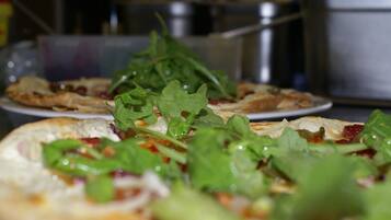 A pizza topped with greens and cheese, with a blurred background of kitchen equipment.