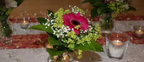 A table setting with a centerpiece of a pink flower, white flowers, and green foliage in a clear glass vase.