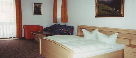 Habitación de hotel con cama de madera, una mesita de noche, escritorio con silla, sofá y un cuadro en la pared.