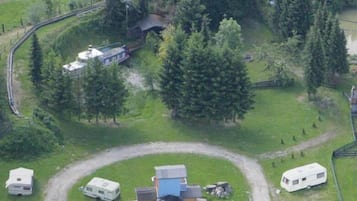 Eine Vogelperspektive zeigt einen Campingplatz mit Wohnmobilen, einem zentralen Gebäude und umliegenden Bäumen.
