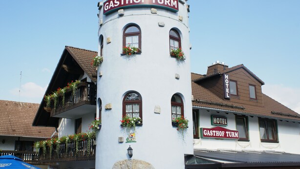 A white building with a sign reading "GASTHOF TURM HOTEL" and a balcony with flower boxes. - Gasthof Turm (Schoenwald)