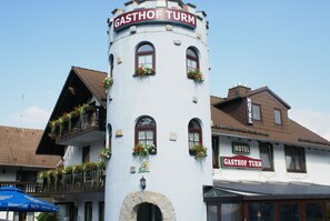 A white building with a sign reading "GASTHOF TURM HOTEL" and a balcony with flower boxes. - Gasthof Turm (Schoenwald)