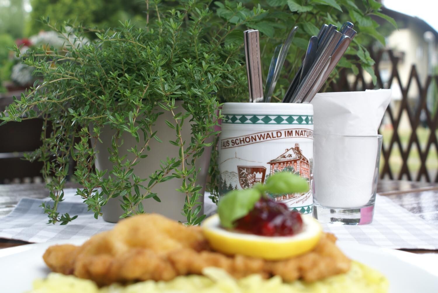 Ein Teller mit gebratenem Essen und einem Zitronenschnitzchen, ein Glas Wasser und ein Behälter mit Besteck.